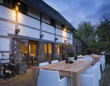 Terras met tafels en stoelen naast een karakteristieke boerderij tijdens schemering