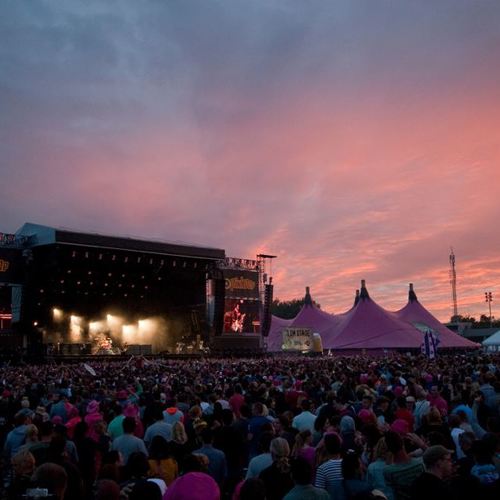 Publiek en podium met daarnaast roze tenten op Pinkpopterrein met rozig schemerlicht