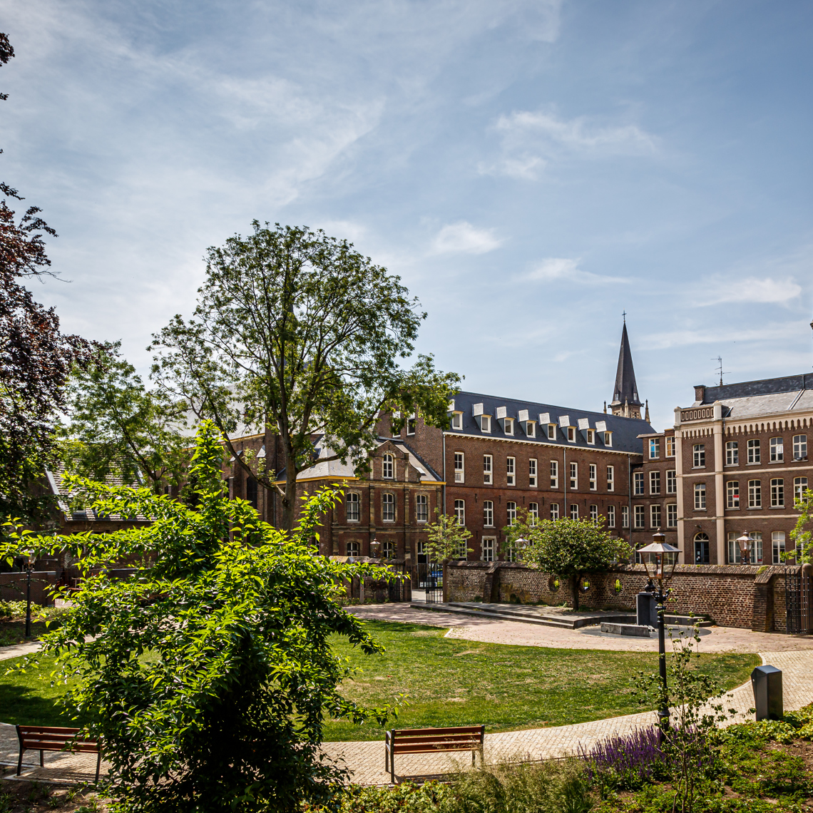 Een ronde tuin met daarachter een indrukwekkend klooster met spitse kerktorens